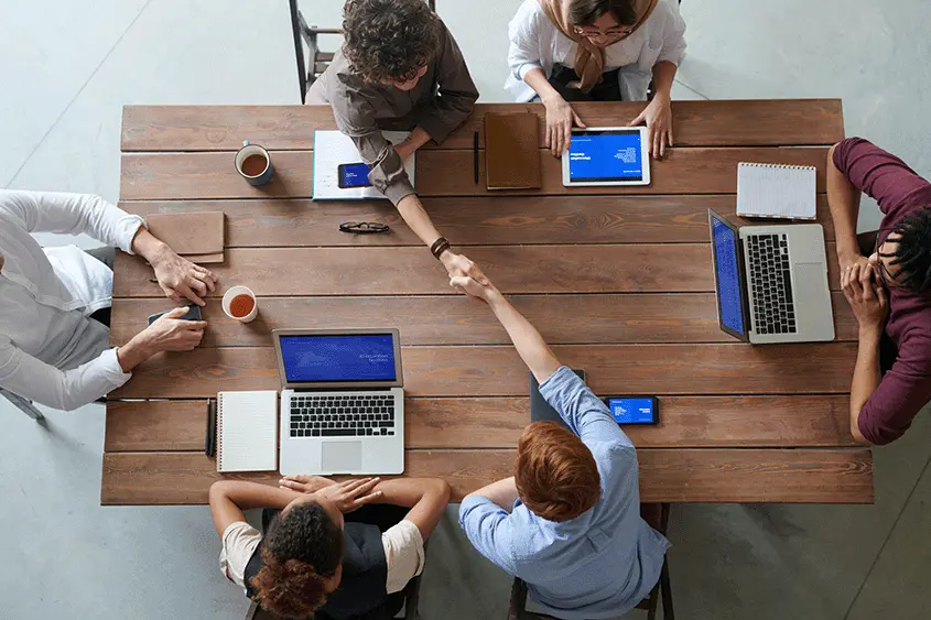 Personer sidder i team rundt om bord og arbejder sammen på pc